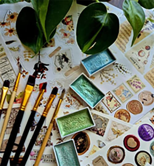 Brushes and small rectangular paint pots sit on top of pieces of paper with stamp sized images on them.