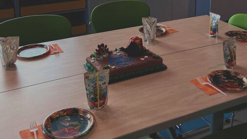 Table set up with chocolate birthday cake in the middle with plates, utensils, napkins, and caprisun