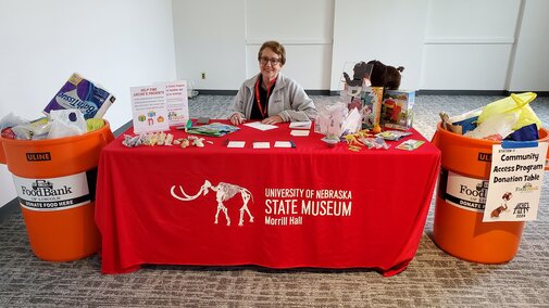 A volunteer sits at a table collecting food donations during an event at the museum.