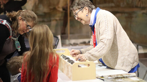 UNSM volunteer showing kids a sauropod bone puzzle.