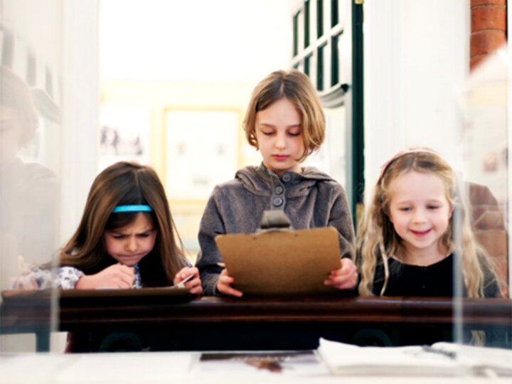 Children study a museum exhibit with clipboards