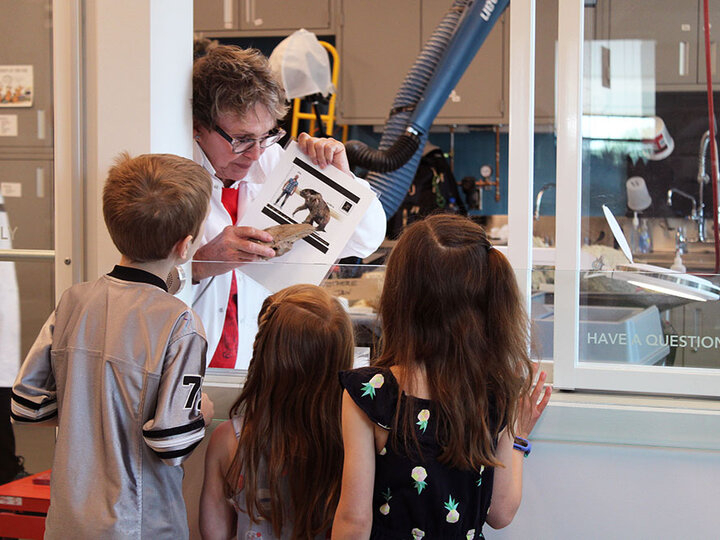 UNSM paleontologist showing three kids a picture in the Visible Lab.