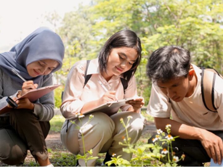 Three pre-teen youth study plants with clipboards in a park