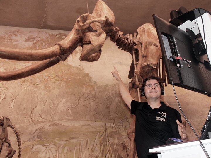 An educator points up at the tusks of Archie the mammoth fossil during a virtual field trip.