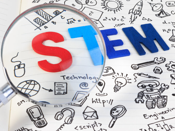 Magnifying glass examines a drawing of science illustrations and the acronym STEM.